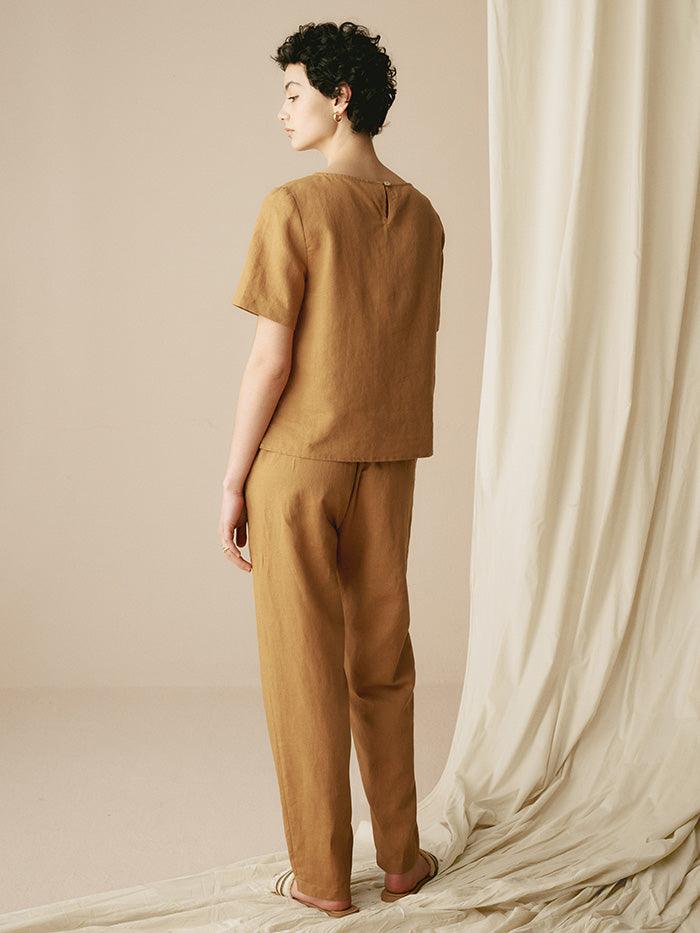 Woman wearing a brown outfit standing in front of a white curtain.
