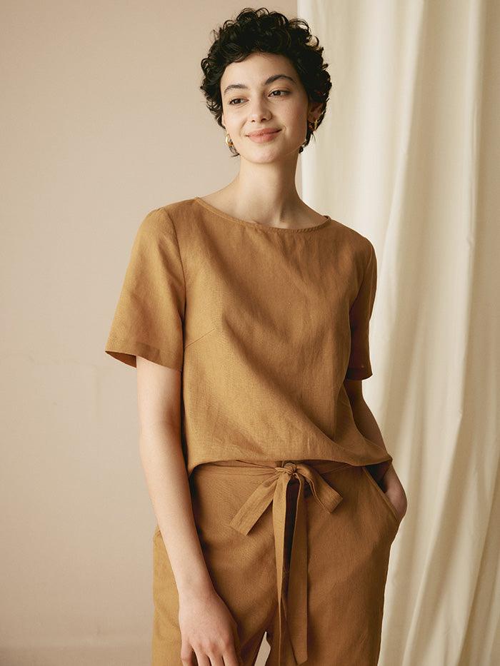 Woman wearing a brown outfit standing against a beige curtain.
