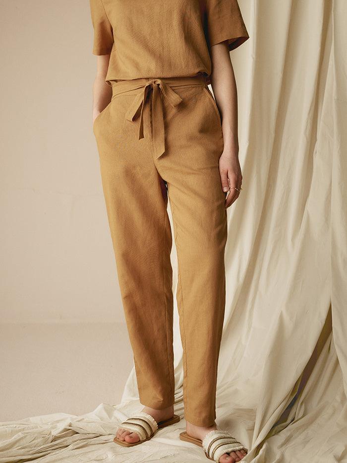 Person wearing a brown outfit with a tie-waist pants and top against a neutral background