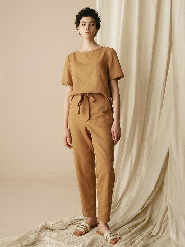 Woman wearing a brown outfit standing against a beige curtain.