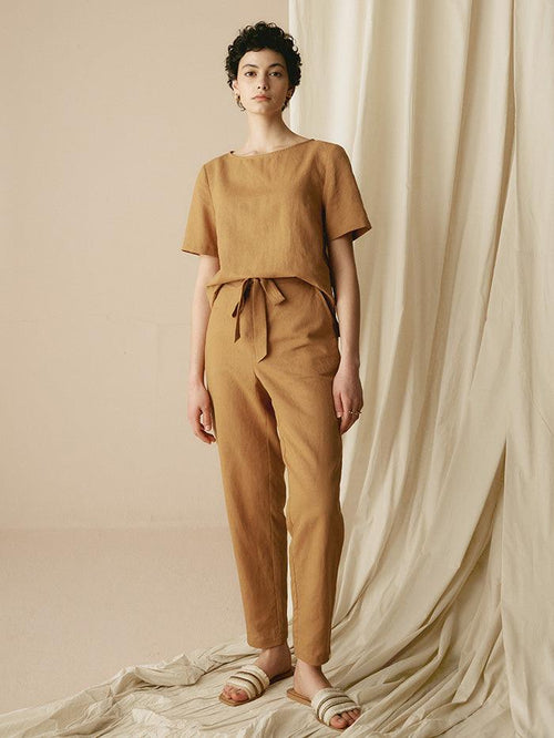 Woman wearing a brown outfit standing against a beige curtain.