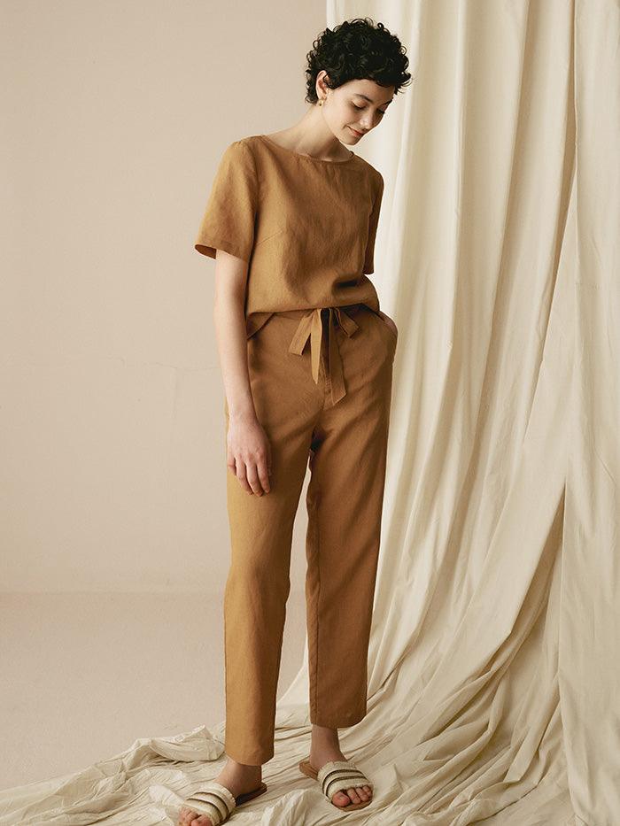 Woman wearing a brown outfit standing against a beige curtain.