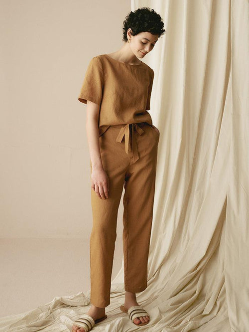 Woman wearing a brown outfit standing against a beige curtain.