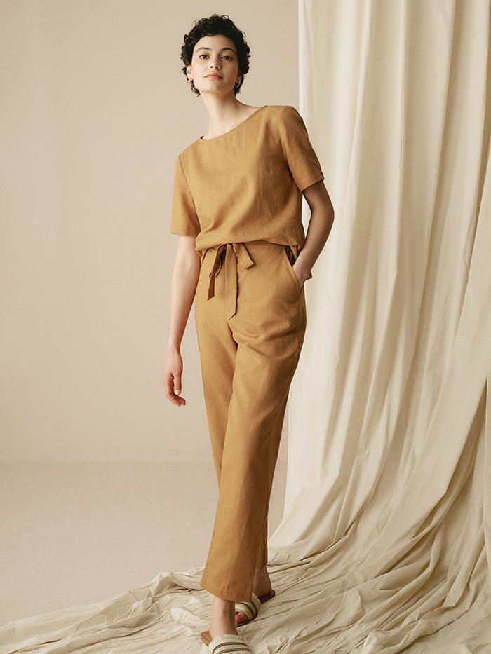 Woman wearing a mustard yellow outfit standing against a draped fabric background