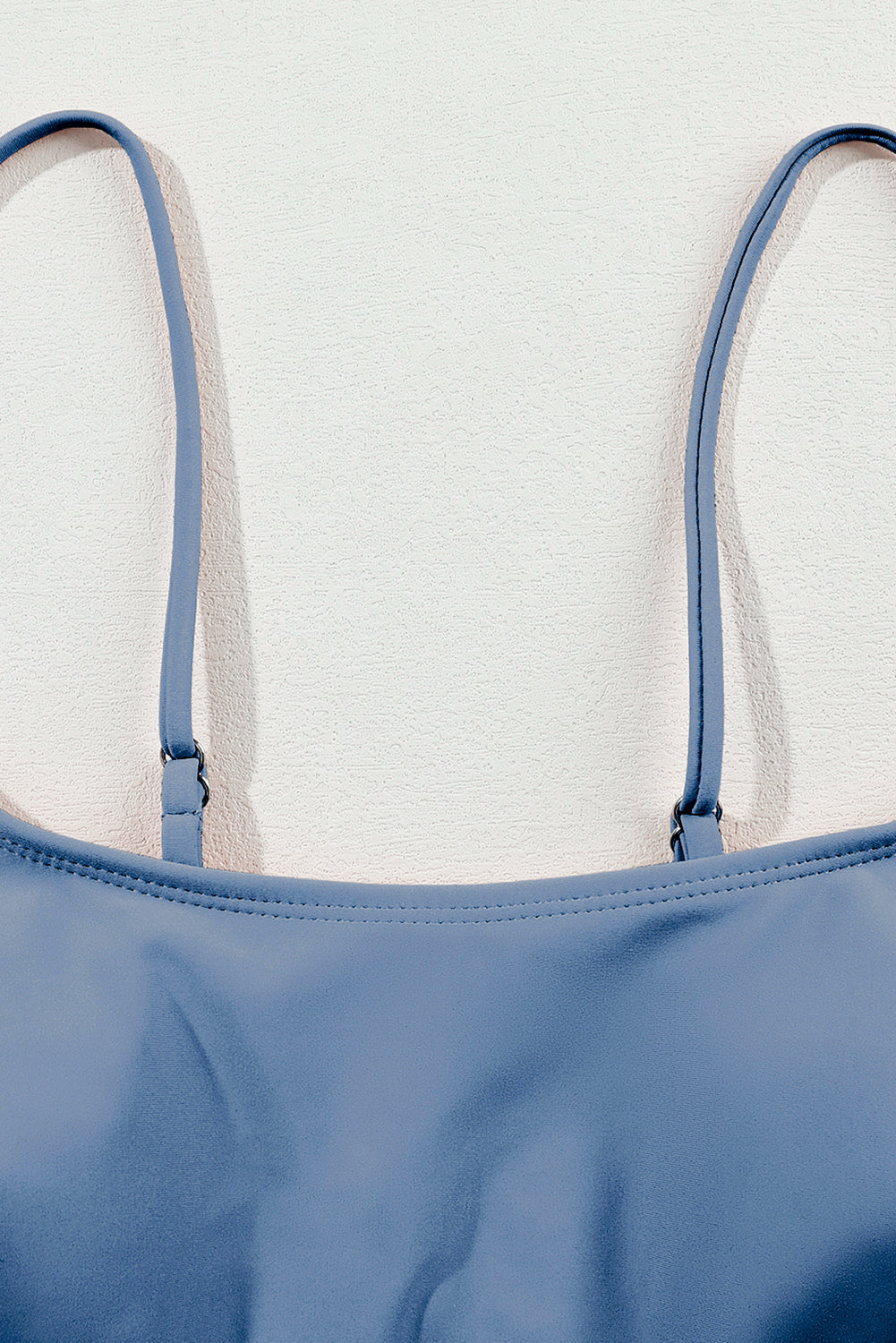 Close-up of a blue swimsuit top with thin straps on a light background