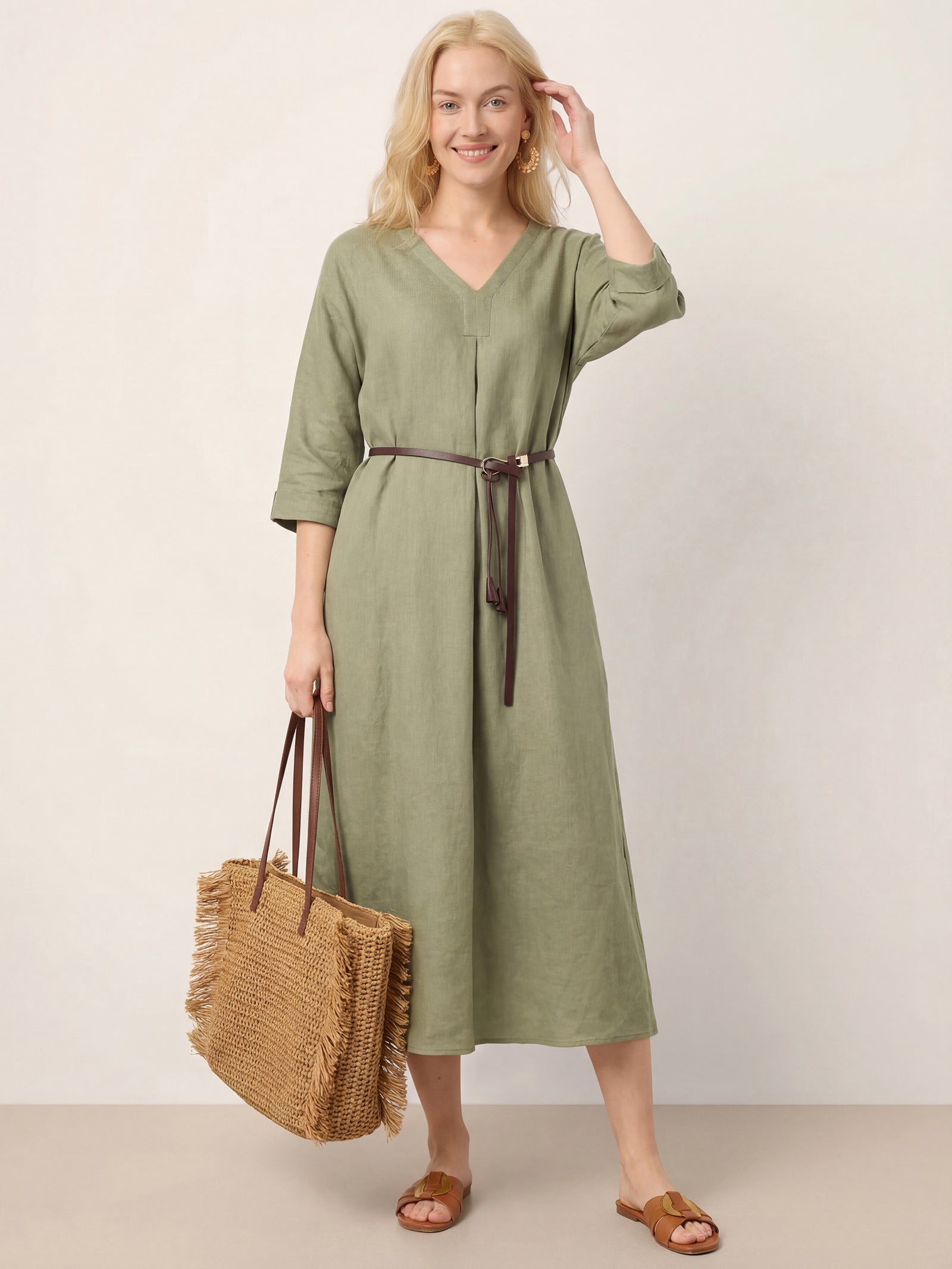 Woman wearing a green dress with a brown belt, holding a woven bag against a plain background
