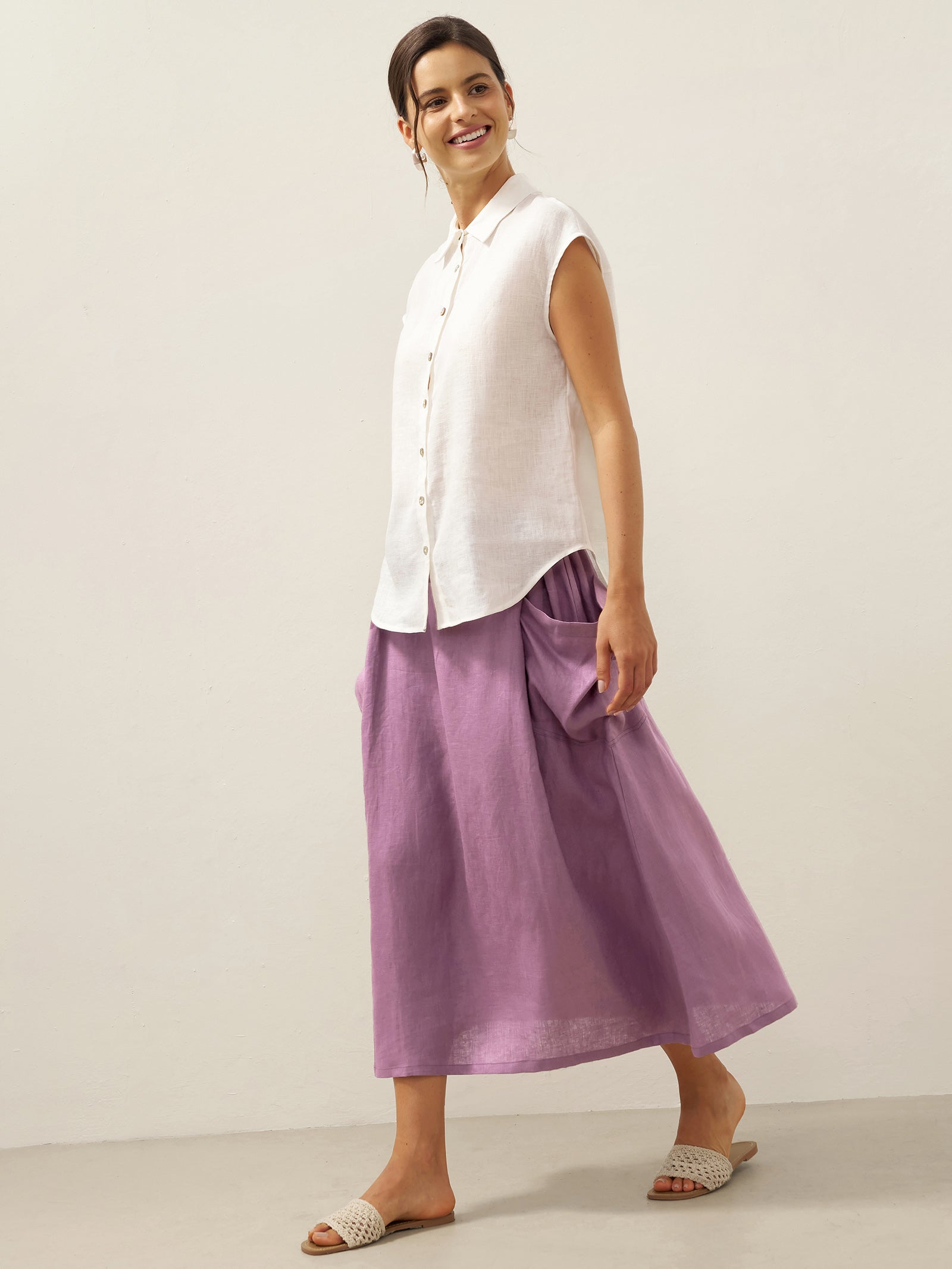 Woman wearing a white sleeveless top and purple skirt on a plain background