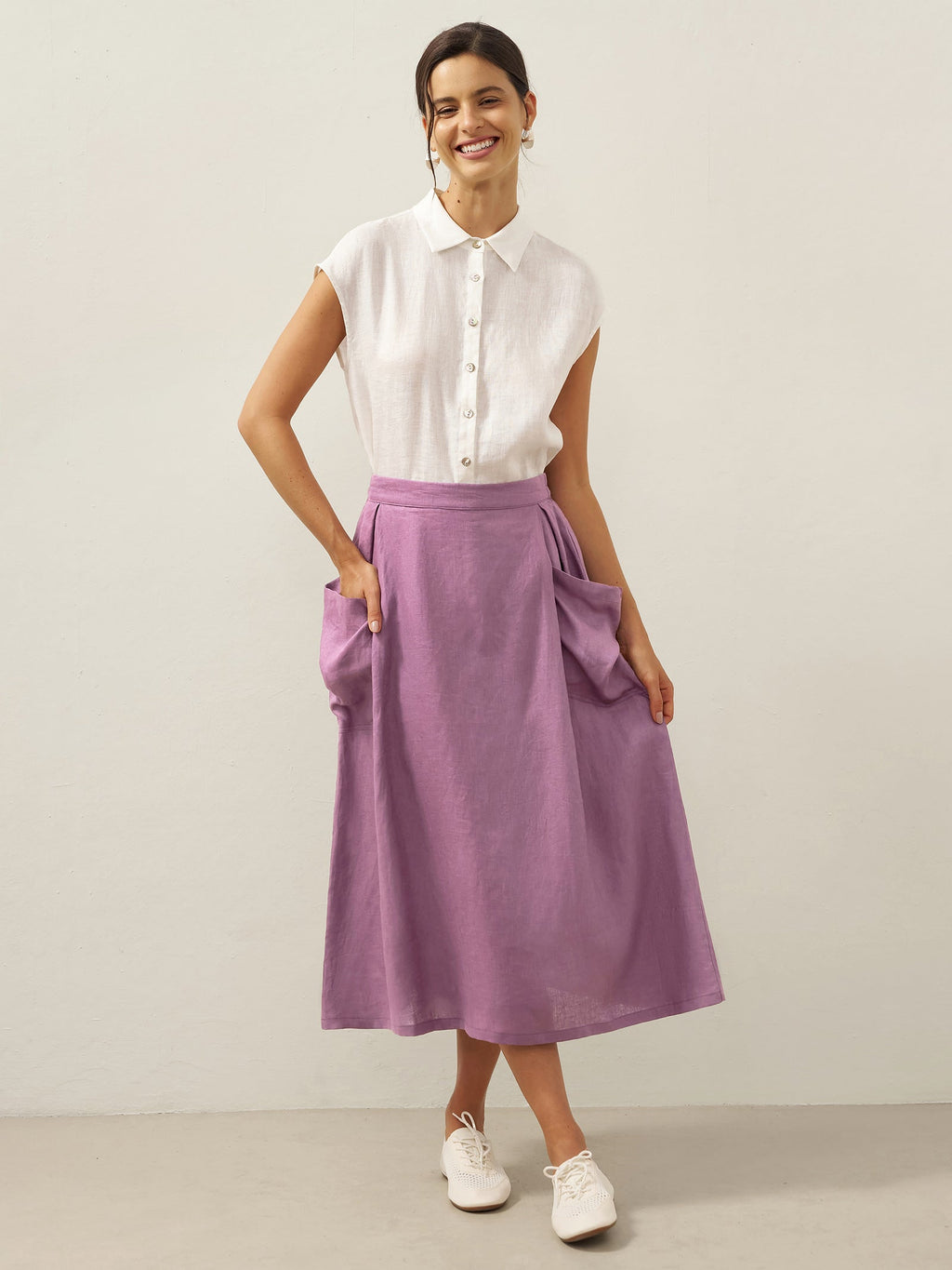 Woman wearing a white blouse and purple skirt against a plain background
