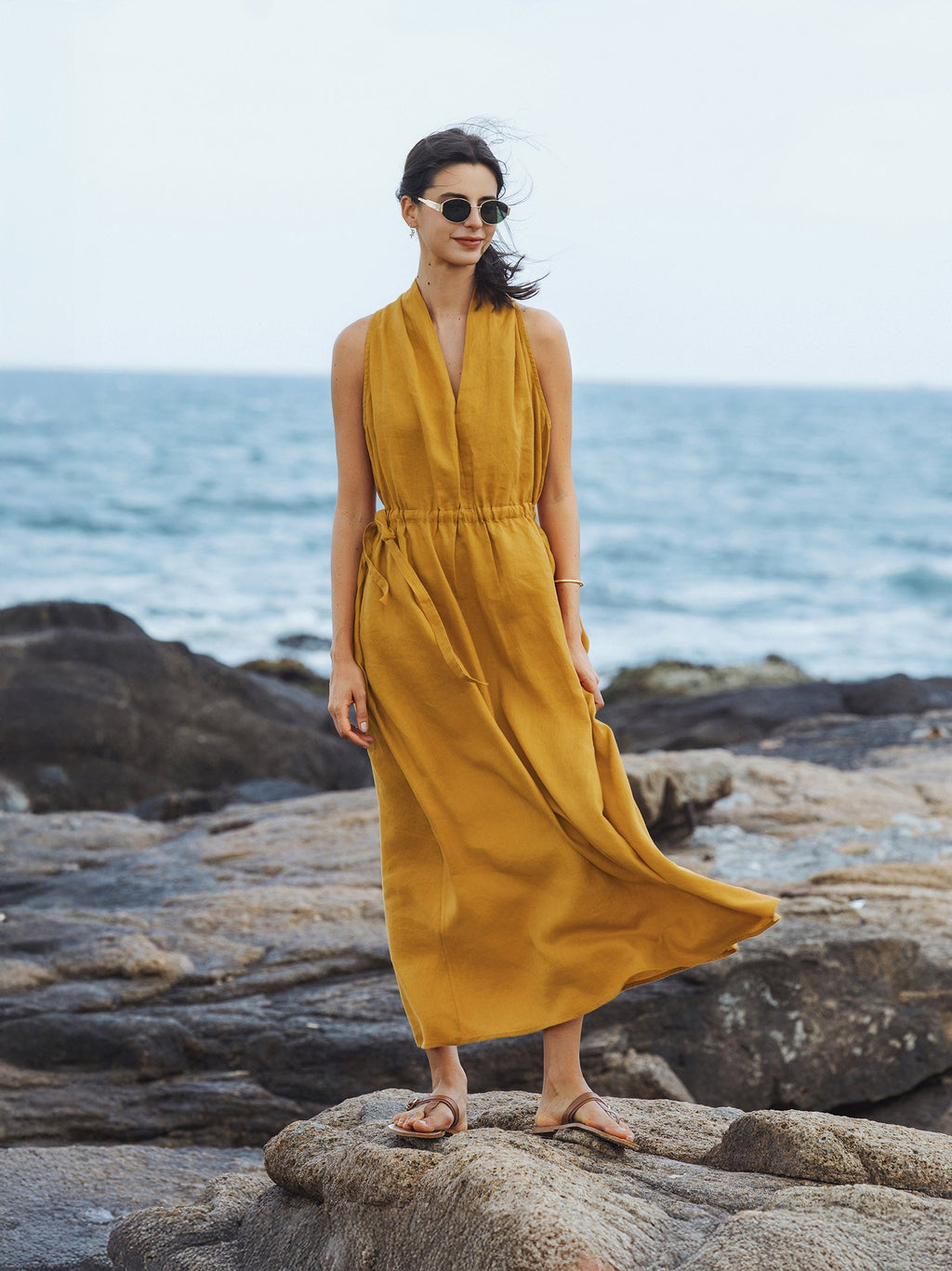 Woman in a yellow dress standing on rocks by the ocean