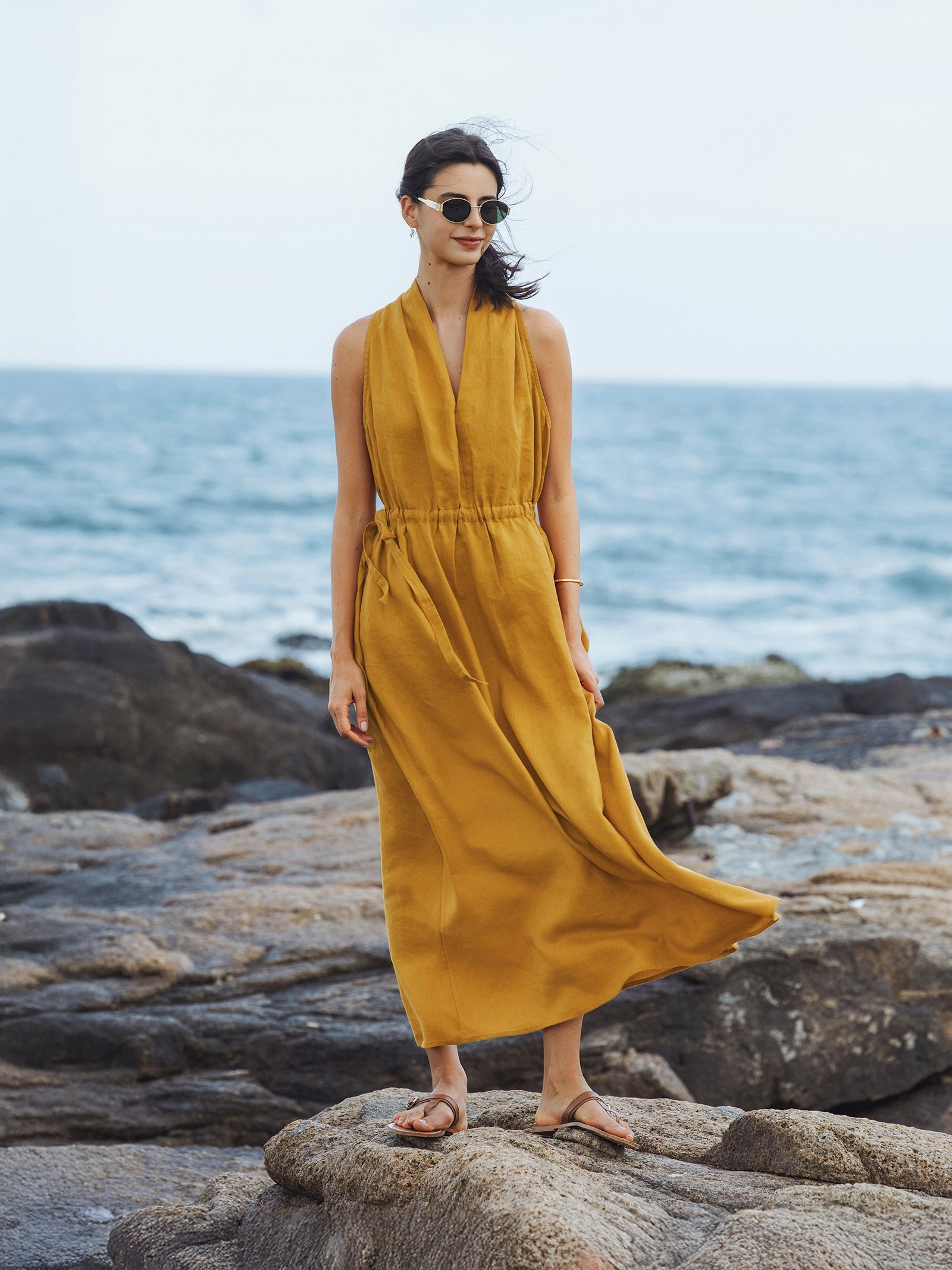 Woman in a yellow dress standing on rocks by the ocean