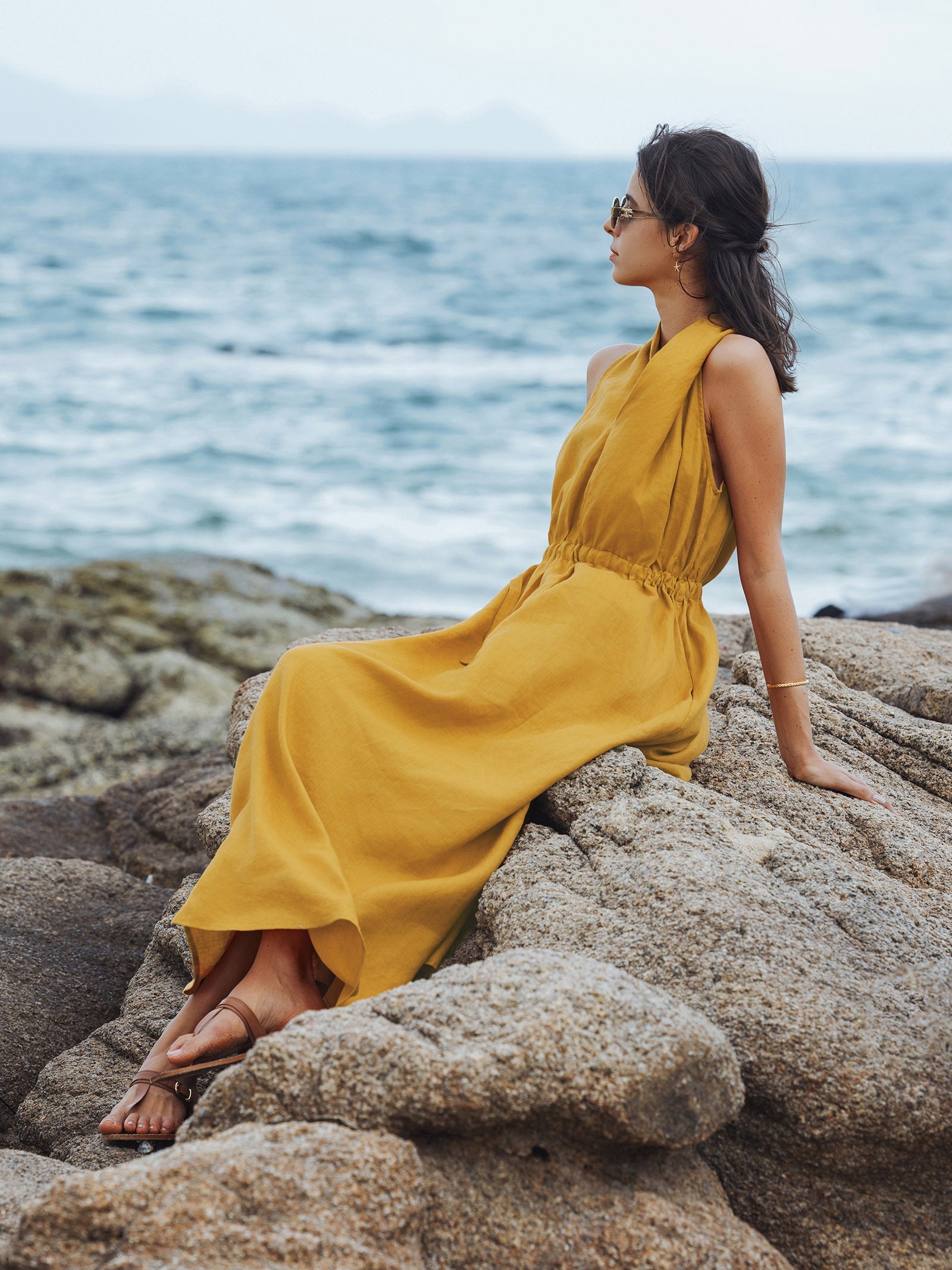 Woman in a yellow dress sitting on rocks by the ocean
