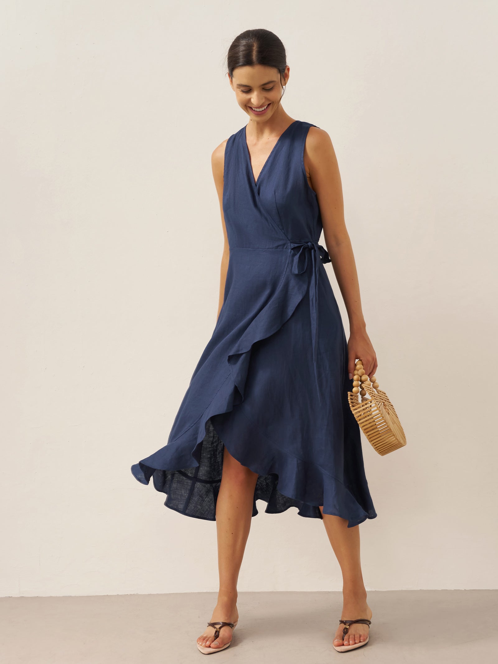 Woman wearing a navy blue dress holding a woven handbag on a plain background