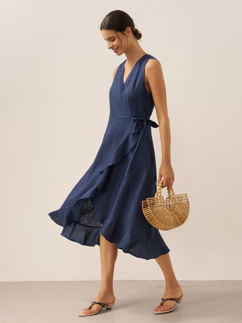 Woman wearing a navy blue dress holding a woven handbag on a plain background