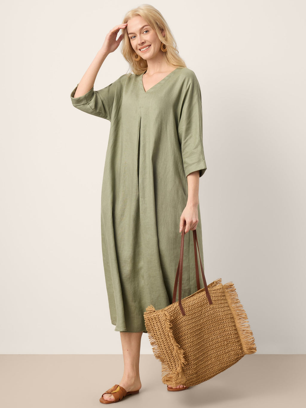 Woman wearing a green dress holding a woven bag against a plain background