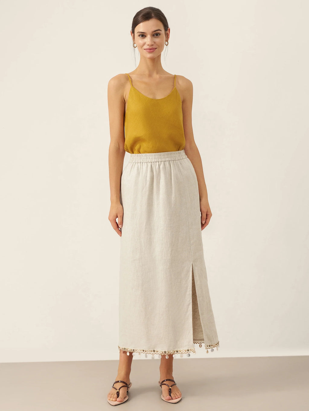 Woman wearing a mustard yellow top and beige skirt on a plain background