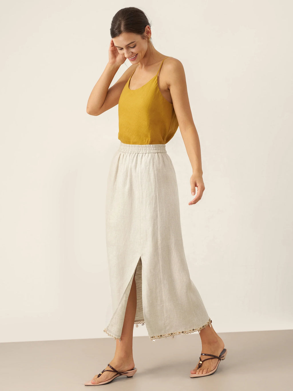 Woman wearing a mustard yellow top and white skirt on a plain background