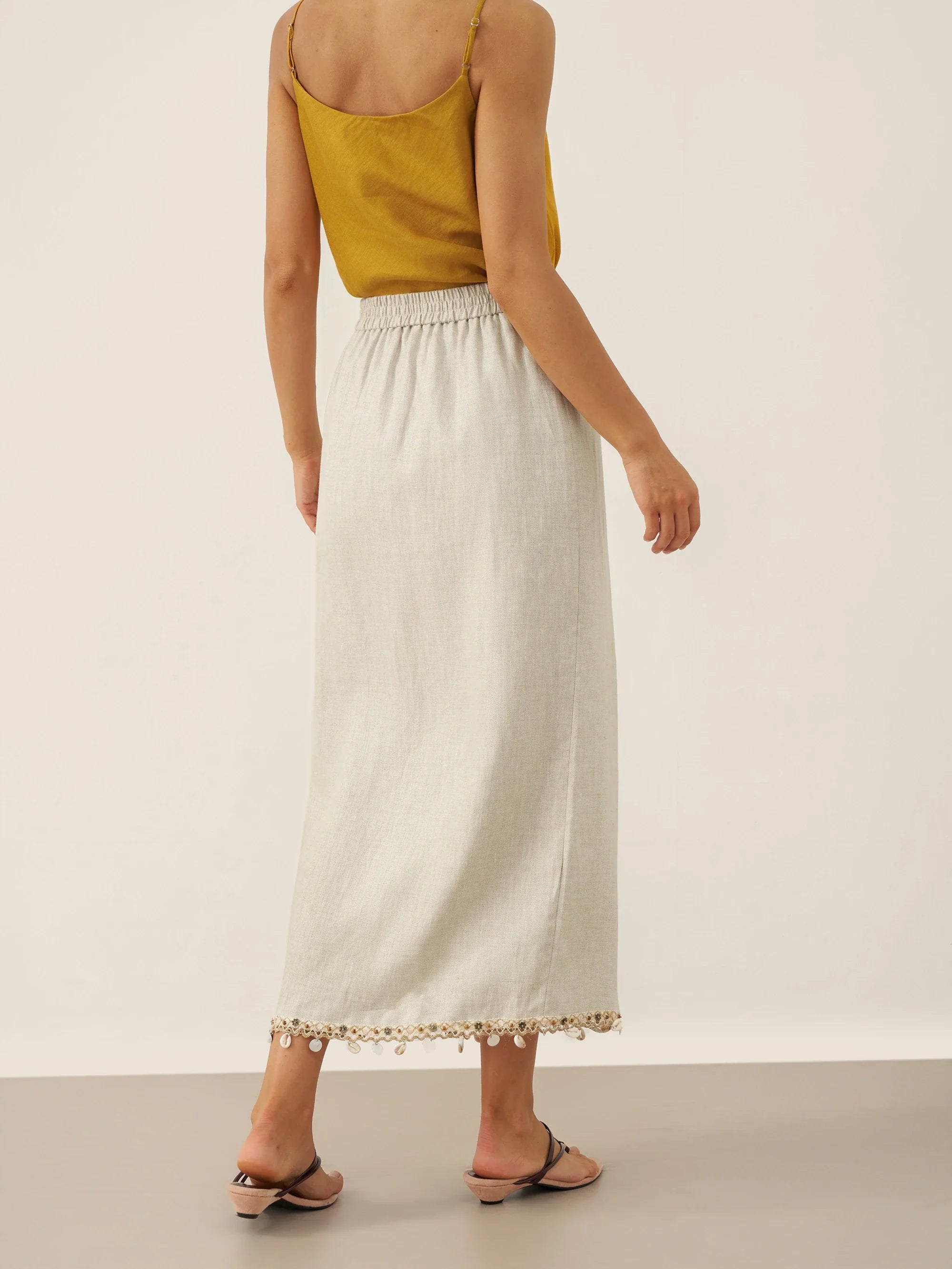 Woman wearing a yellow top and white skirt with lace trim on a plain background