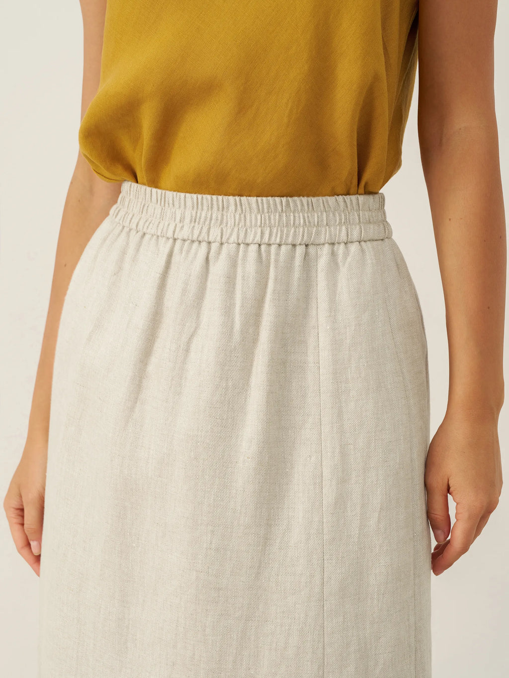Person wearing a mustard yellow top and beige skirt on a plain background