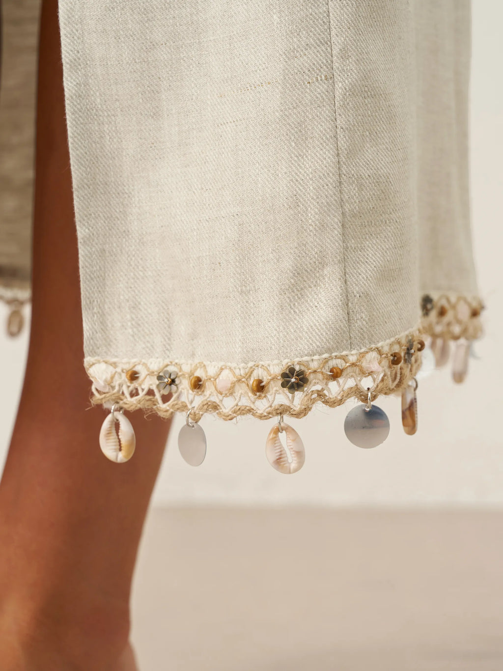 Close-up of a light-colored fabric with decorative trim featuring beads and shells on a neutral background.