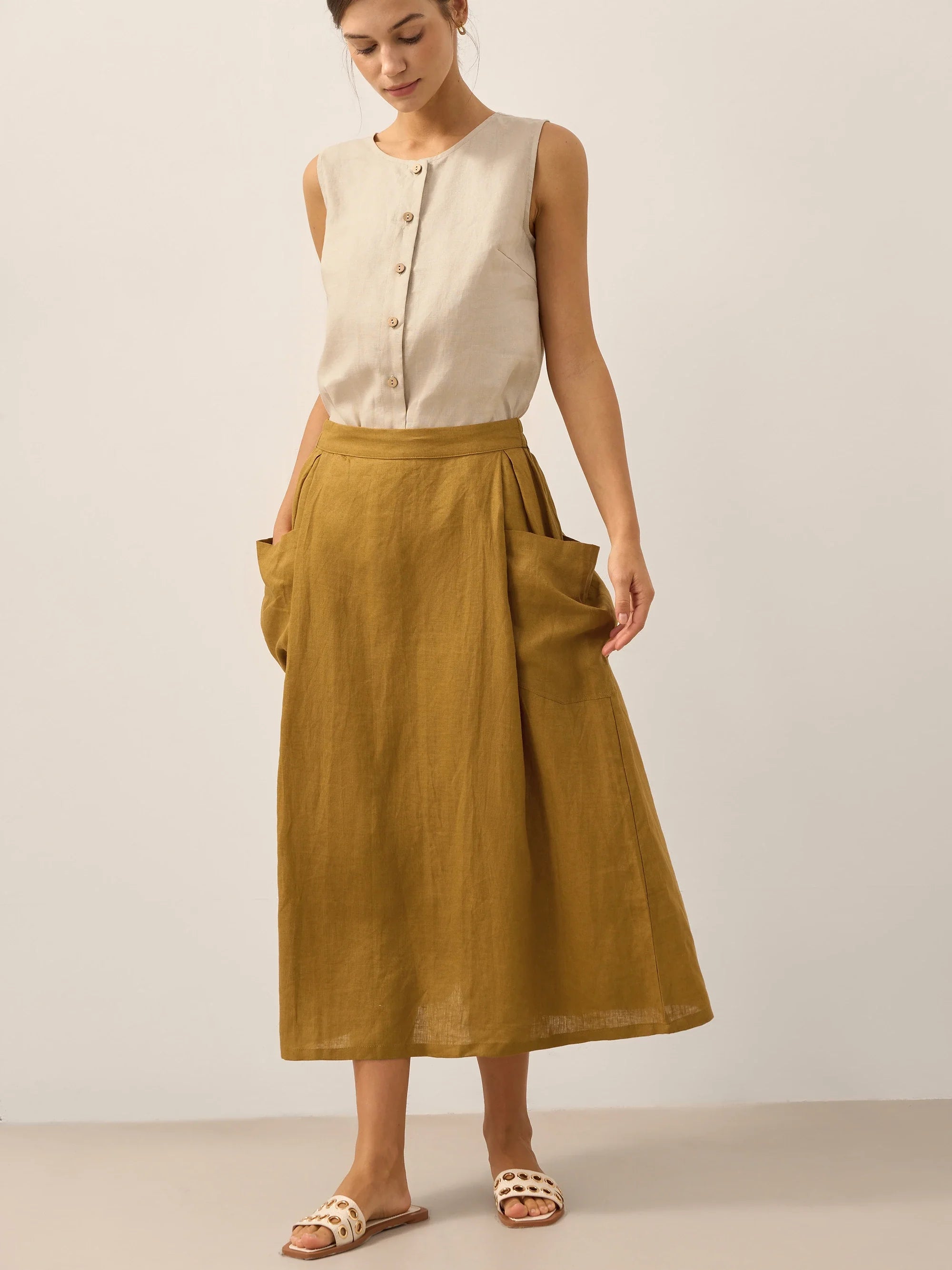 Woman wearing a beige sleeveless top and mustard yellow skirt on a plain background