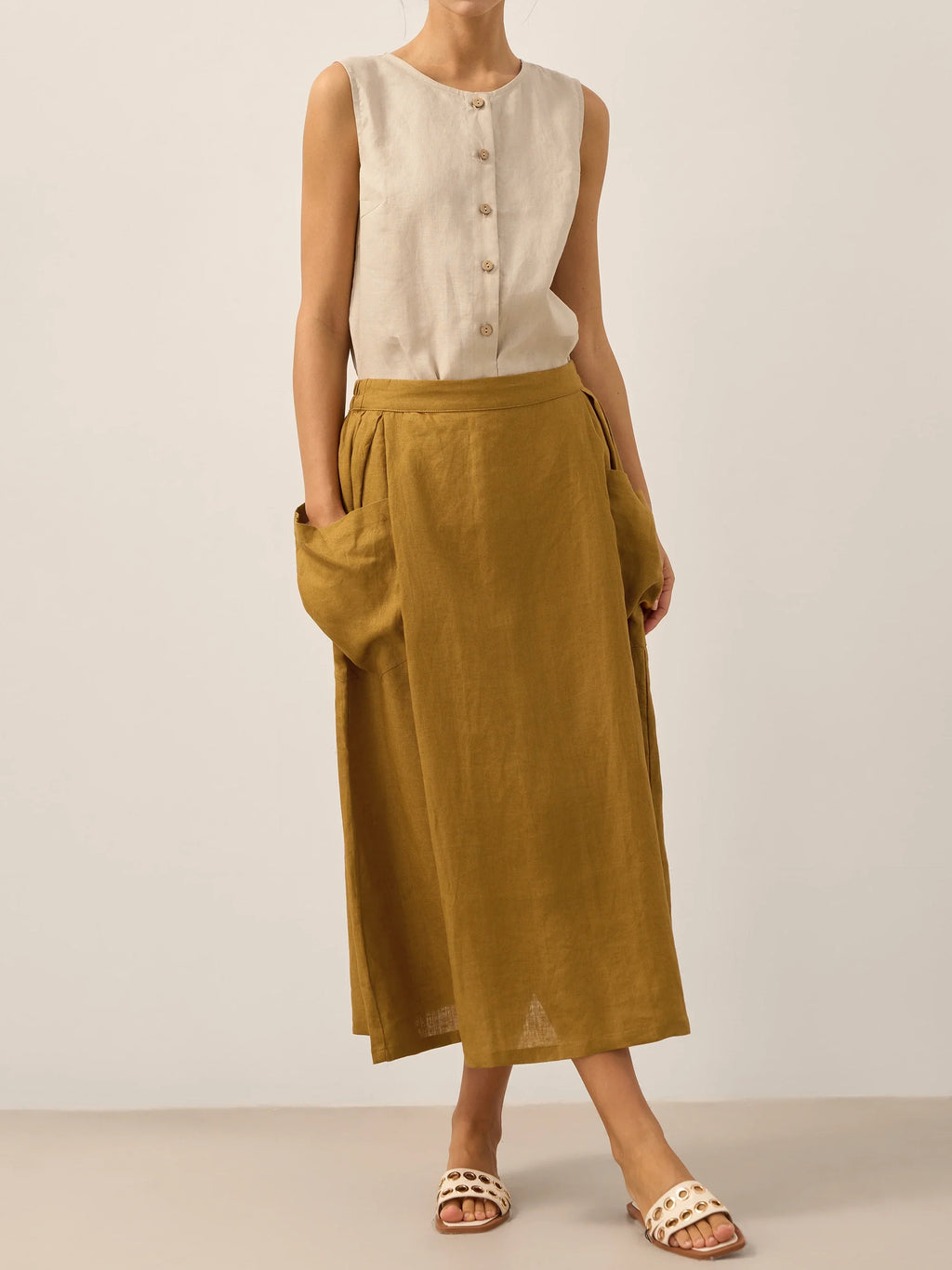 Person wearing a sleeveless beige top and mustard yellow skirt on a plain background