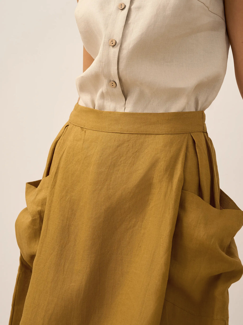 Person wearing a beige button-up shirt and mustard yellow pants on a plain background