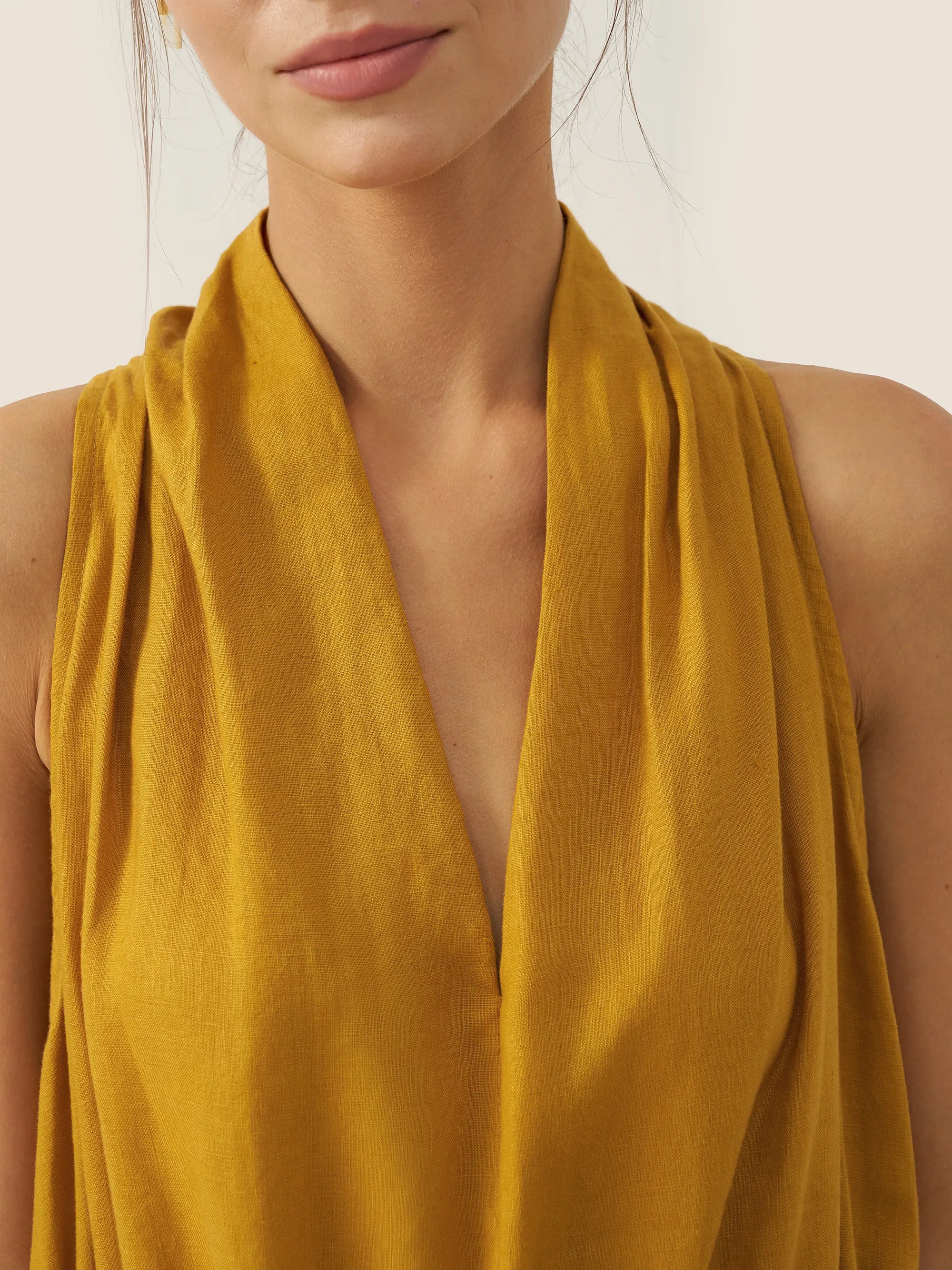 Mustard yellow sleeveless top worn by a person on a plain background