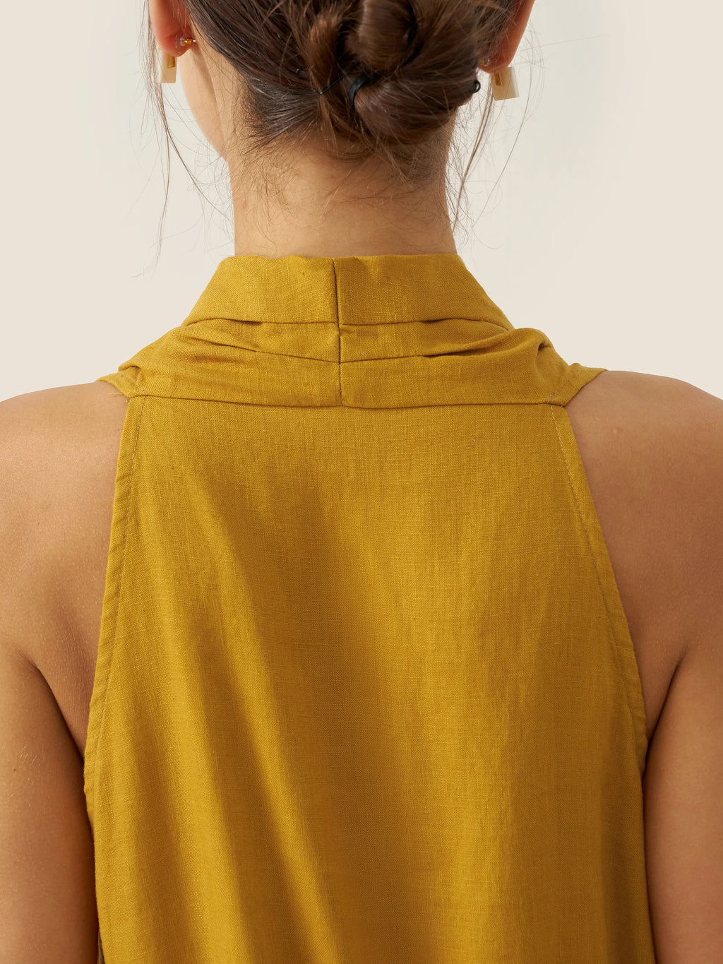 Yellow sleeveless top worn by a person on a plain background