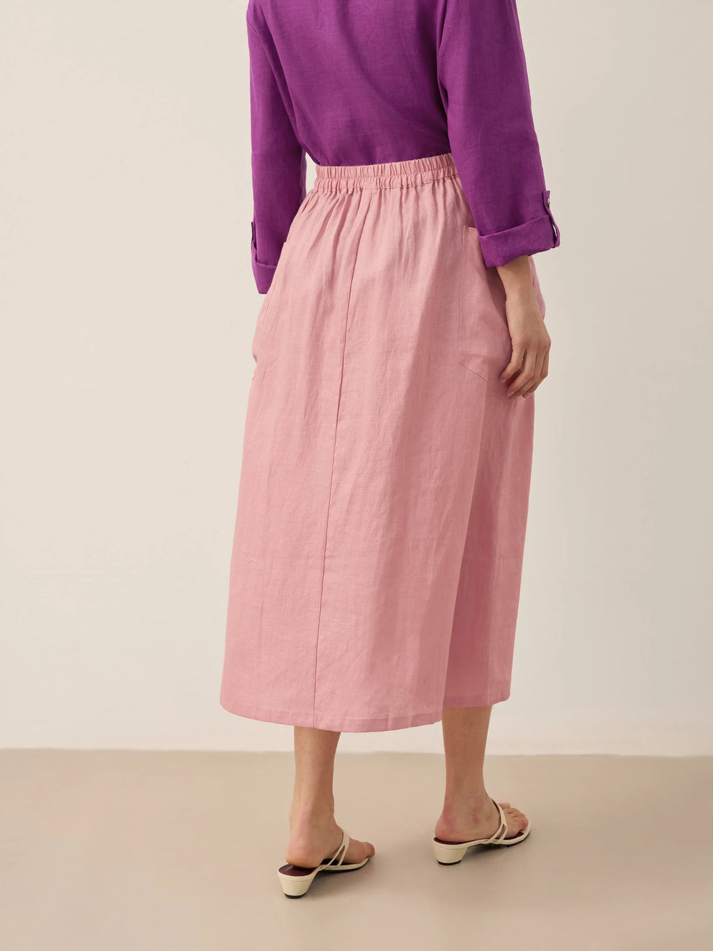 Person wearing a purple top and pink skirt on a beige background
