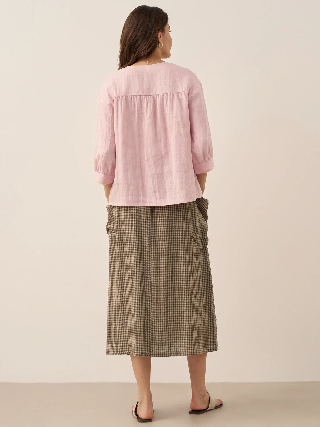 Woman wearing a pink blouse and plaid skirt on a beige background