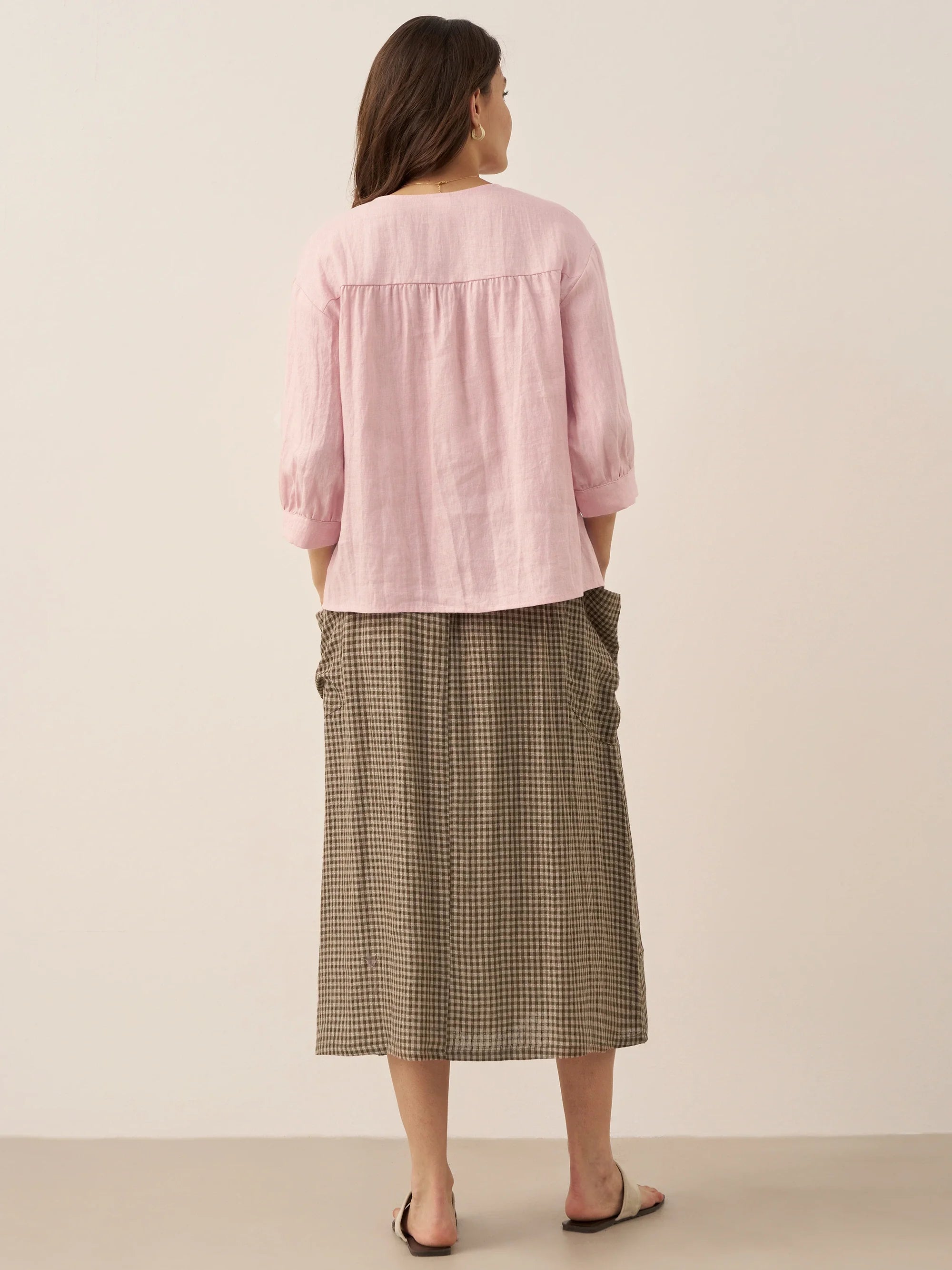 Woman wearing a pink blouse and plaid skirt on a beige background