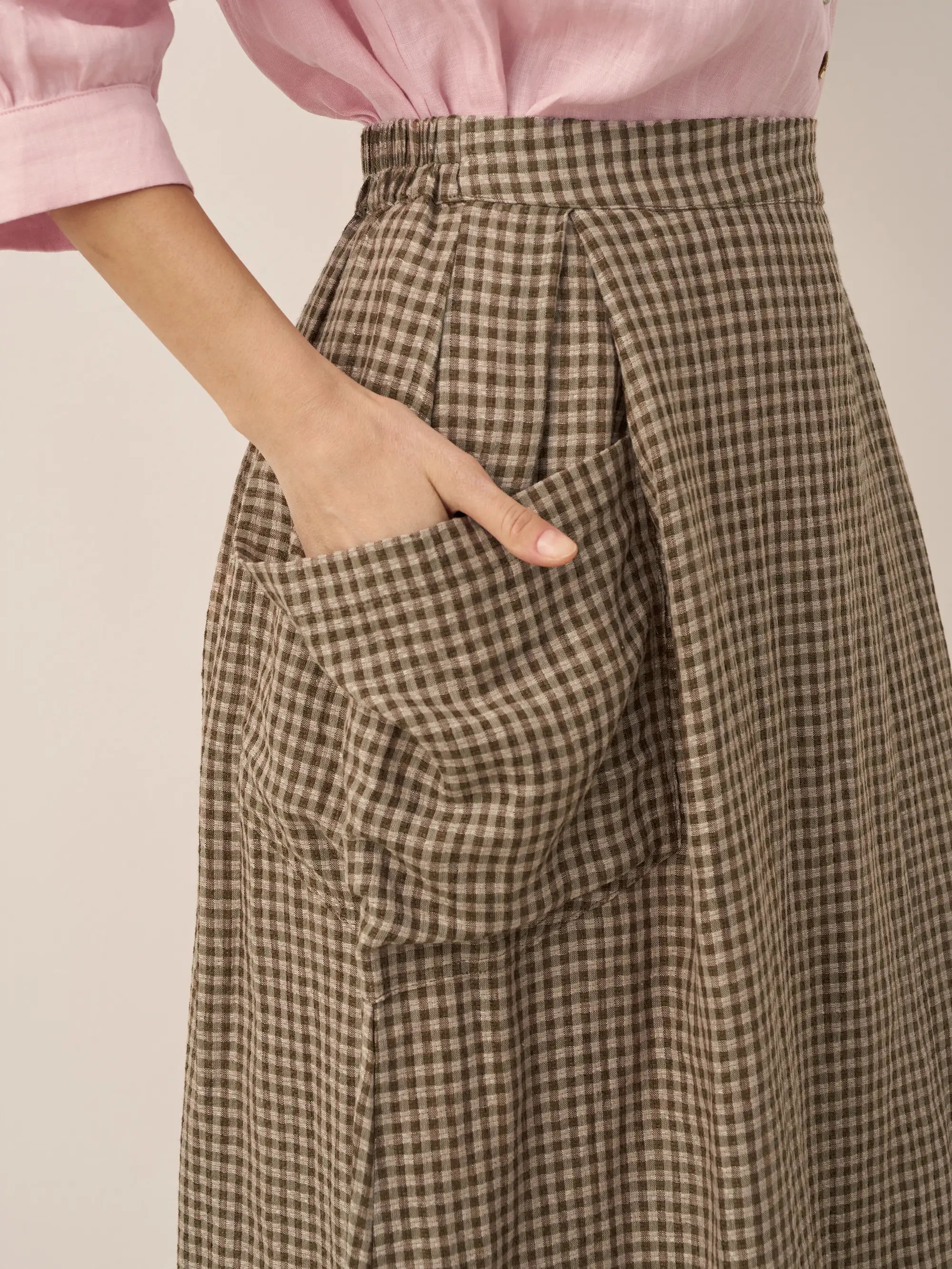 Brown checkered skirt with a pink top on a neutral background