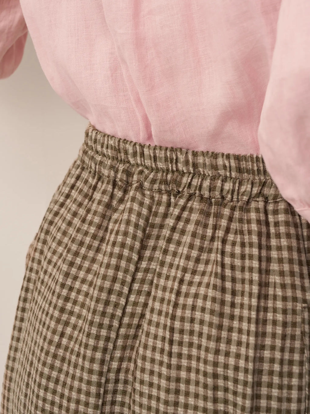 Brown checkered pants with a pink blouse on a neutral background