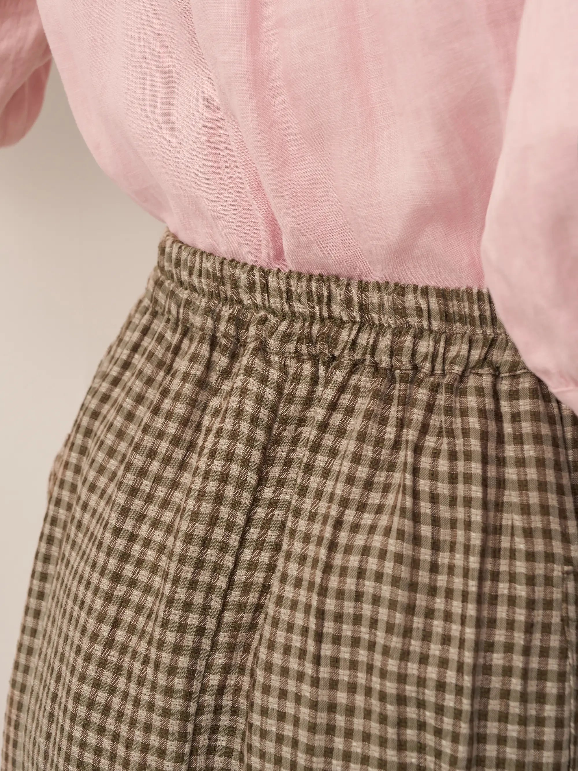 Brown checkered pants with a pink blouse on a neutral background