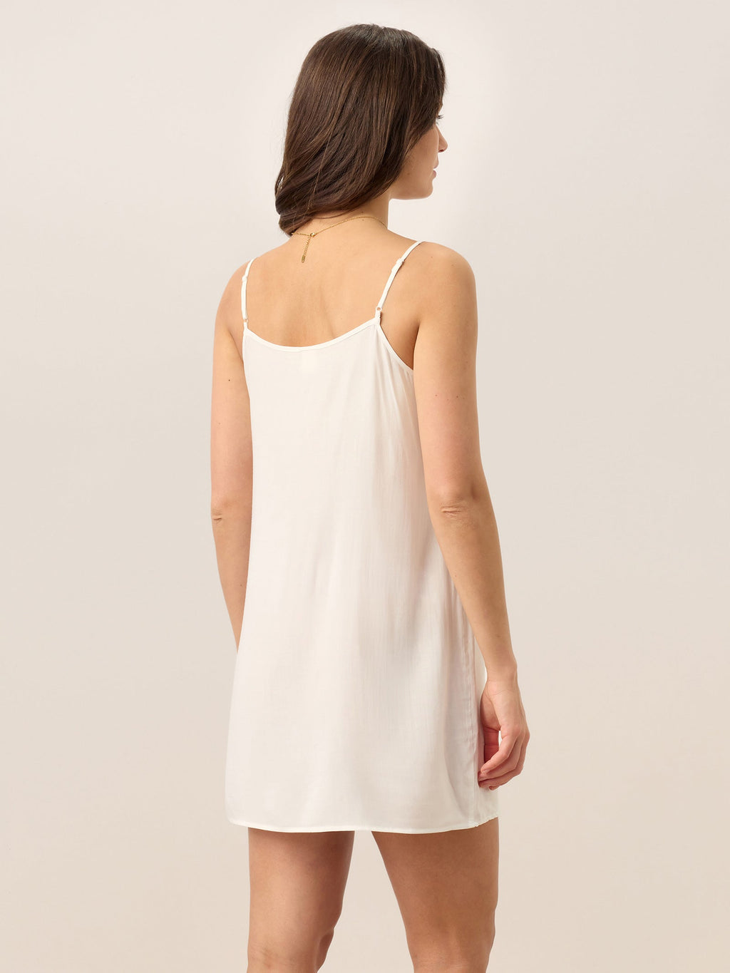 Woman wearing a white slip dress against a plain background