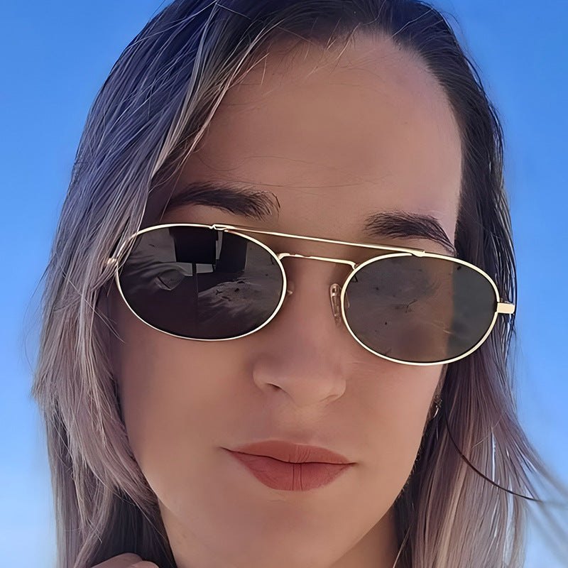 Close-up of a person wearing gold-framed sunglasses with a clear blue sky background