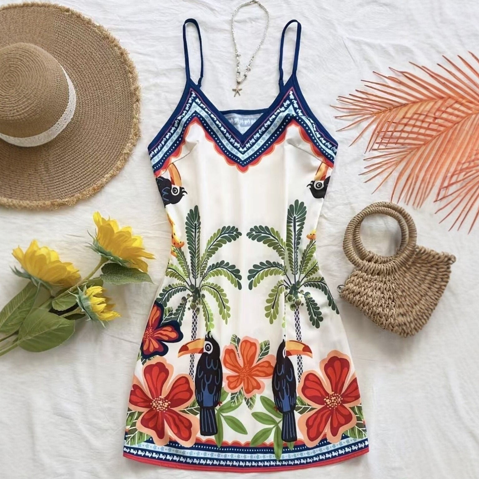 Colorful dress with tropical patterns, straw hat, and bag on a white background