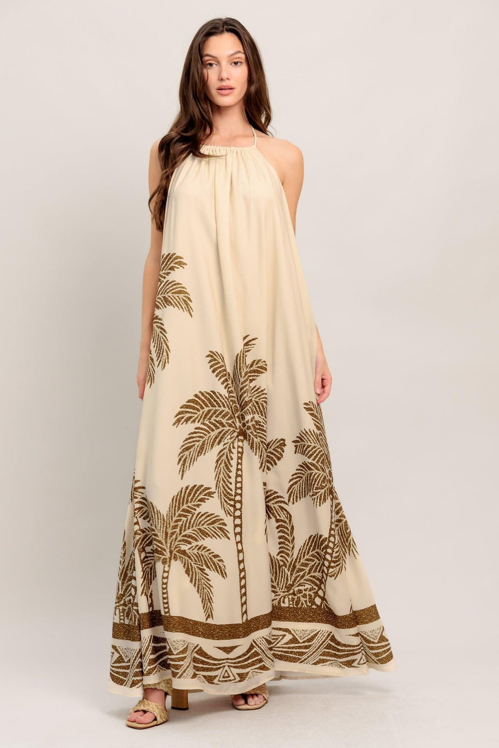 Woman wearing a long beige dress with palm tree patterns on a white background