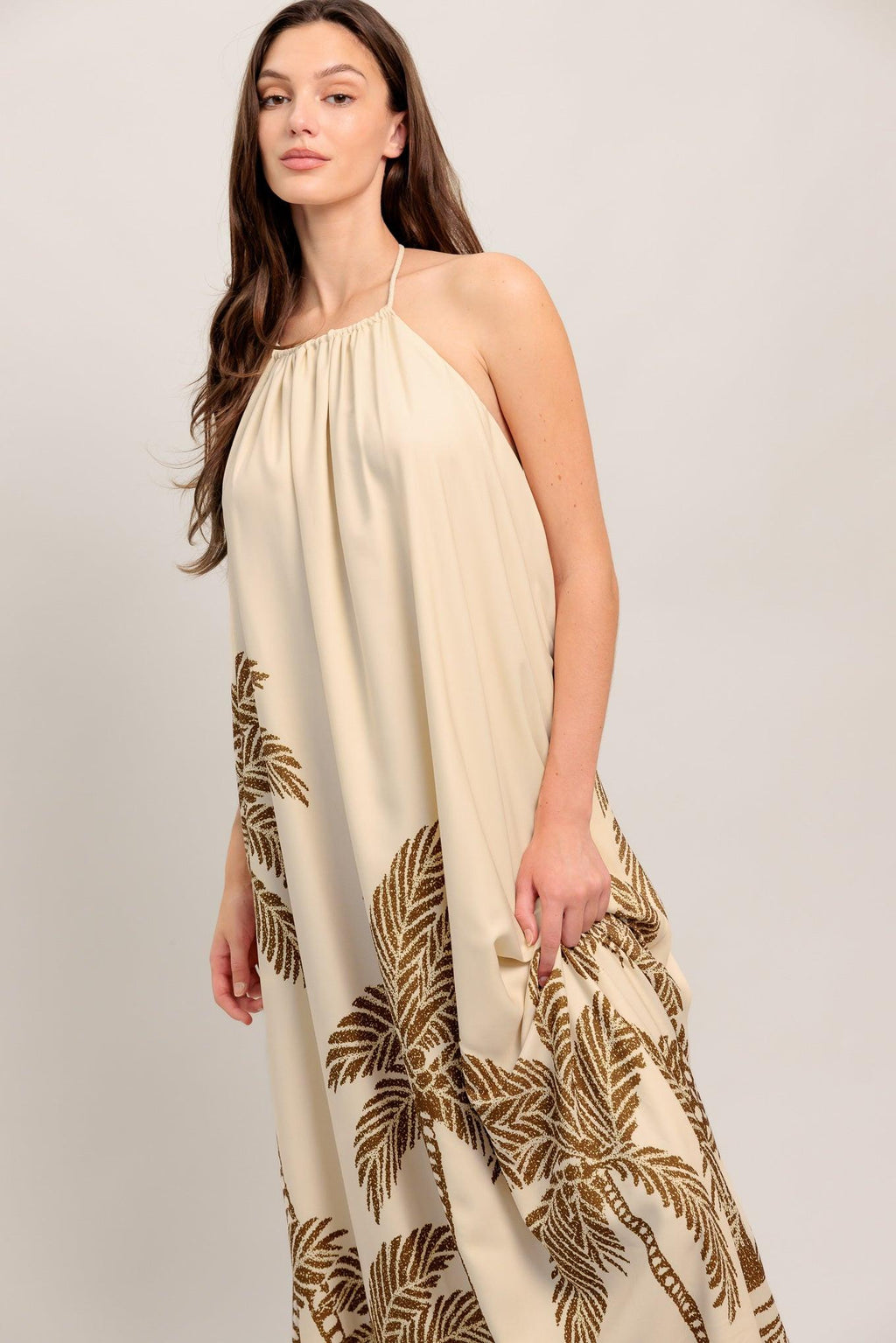 Woman wearing a beige dress with gold leaf patterns on a plain background