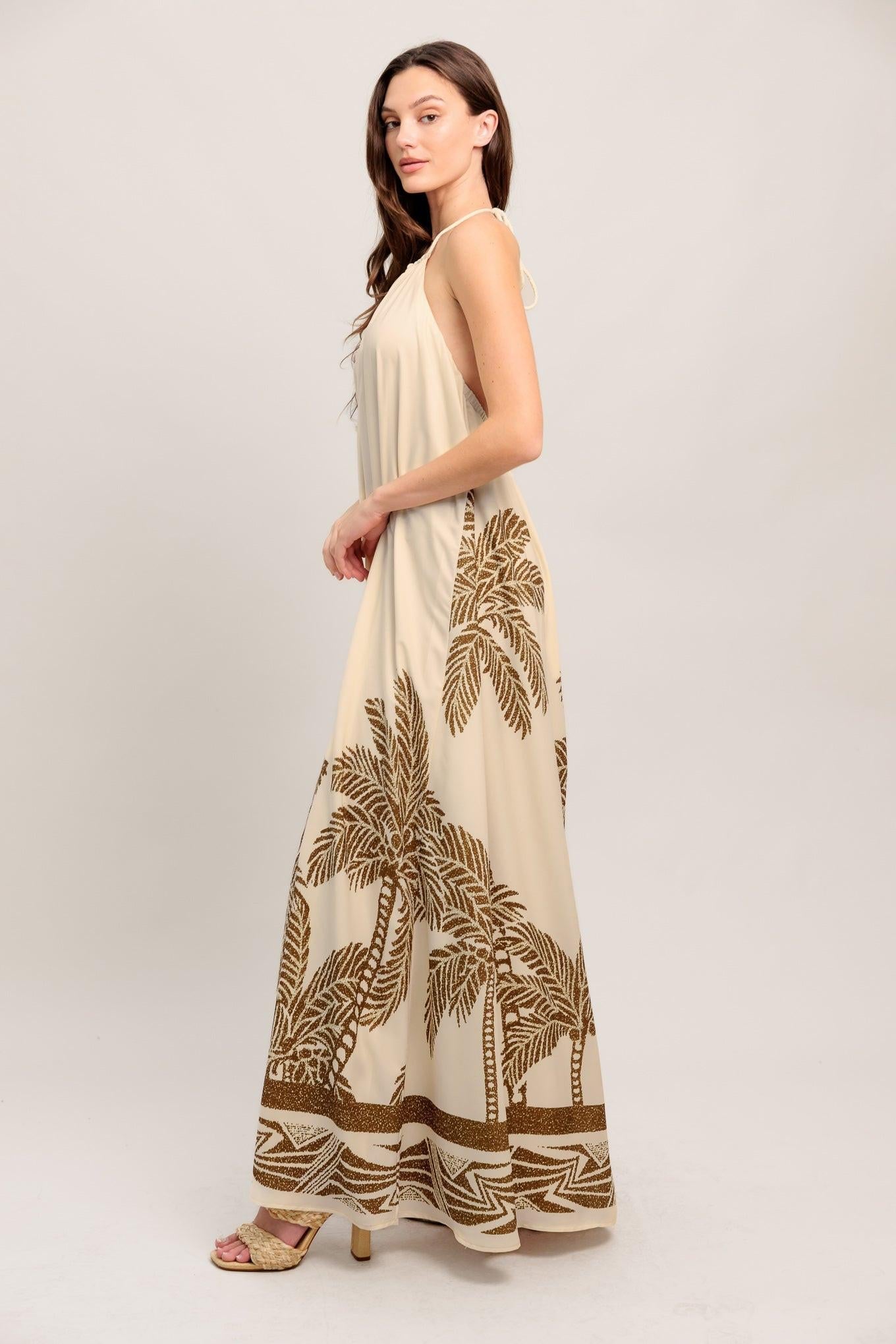 Woman wearing a beige maxi dress with palm tree patterns on a white background