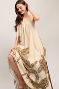Woman wearing a beige dress with gold leaf patterns on a plain background