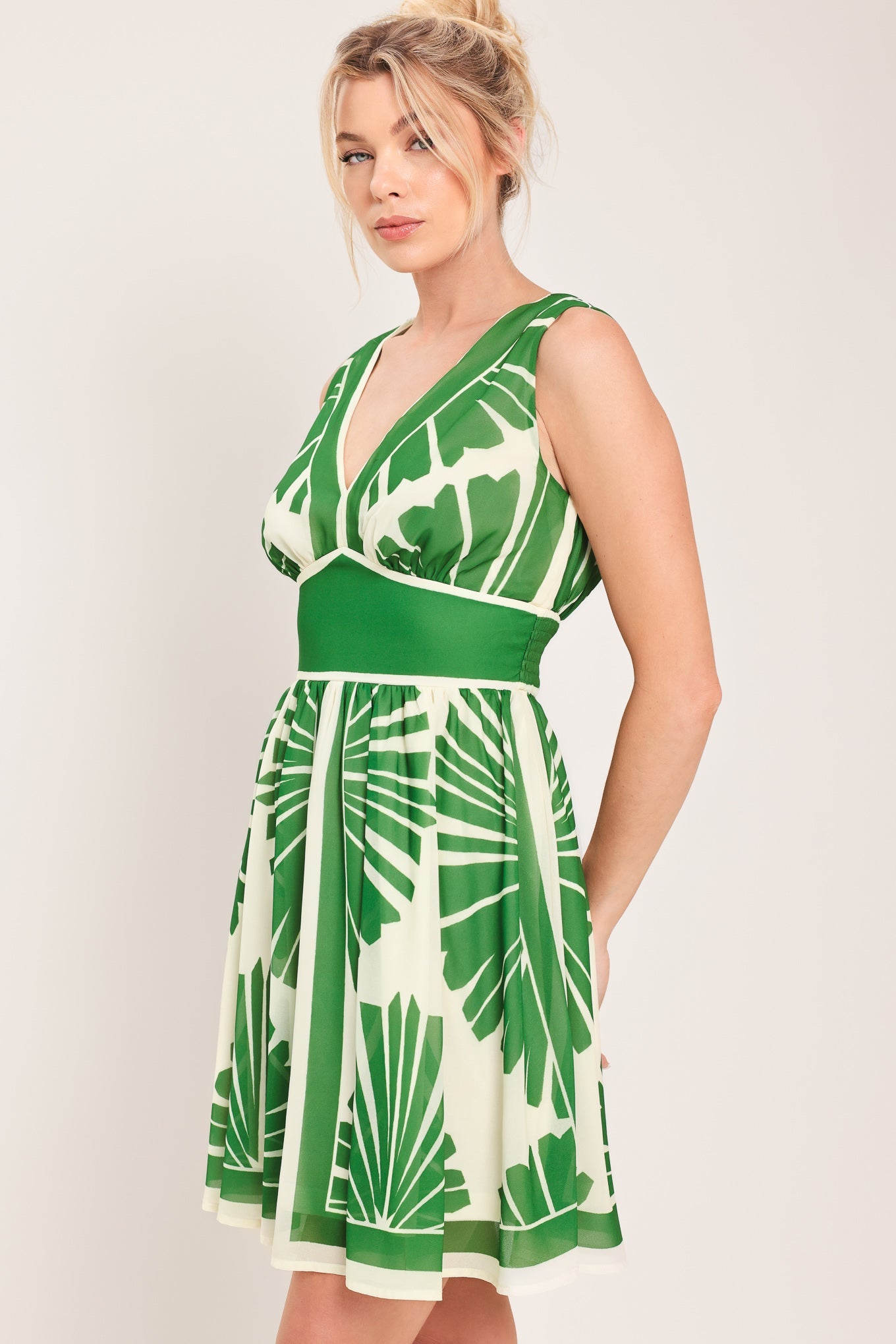 Woman wearing a green and white leaf-patterned dress on a plain background