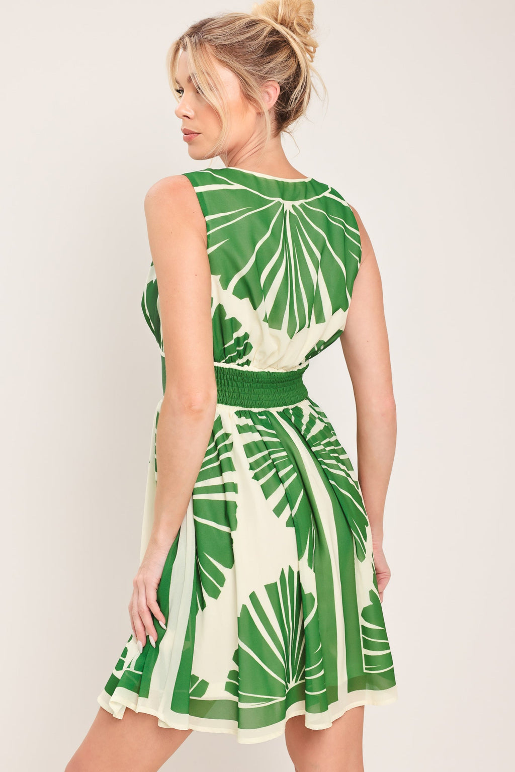 Woman wearing a green and white dress with leaf pattern on a plain background