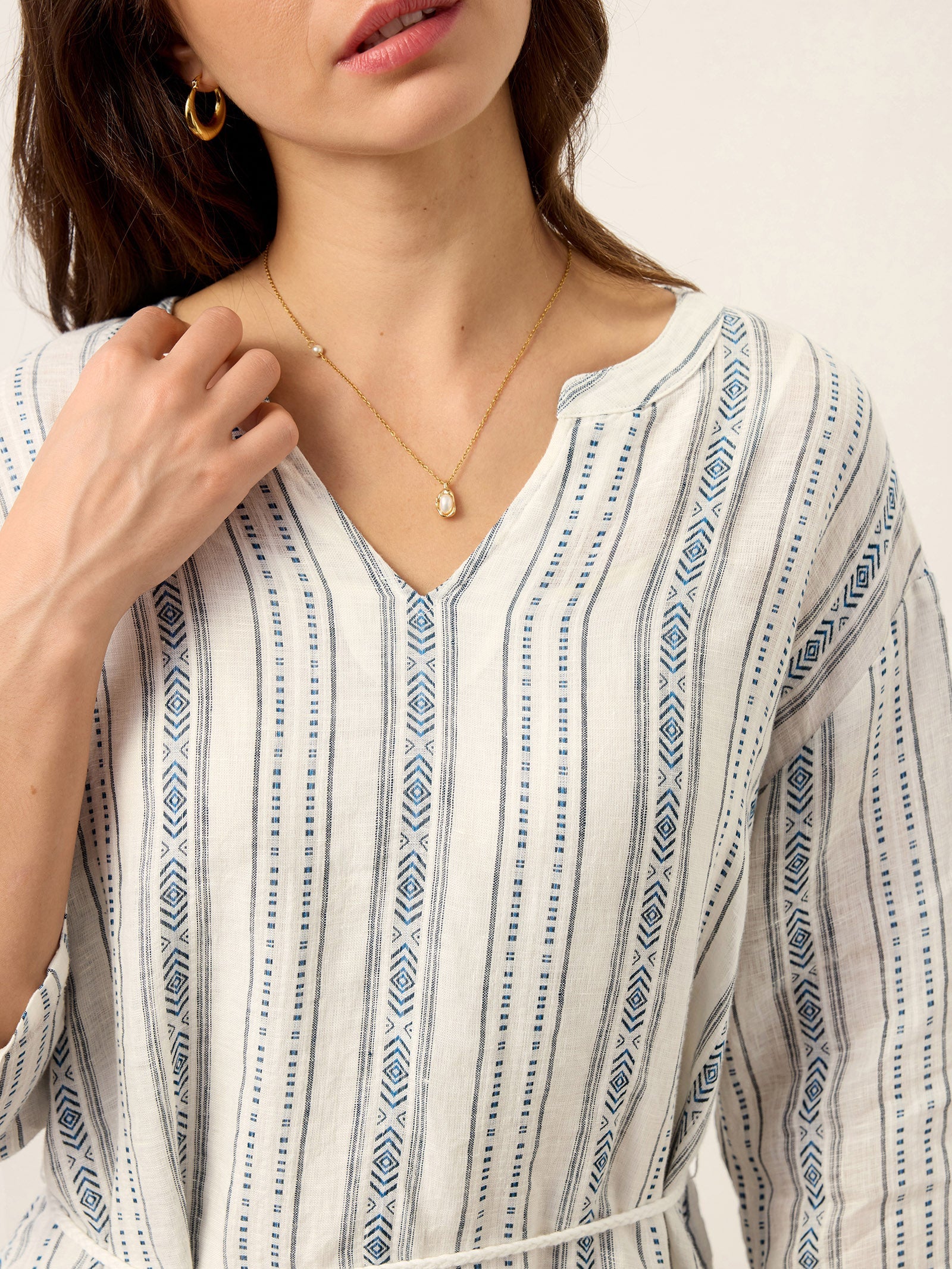 Close-up of a person wearing a white and blue patterned top with a necklace.