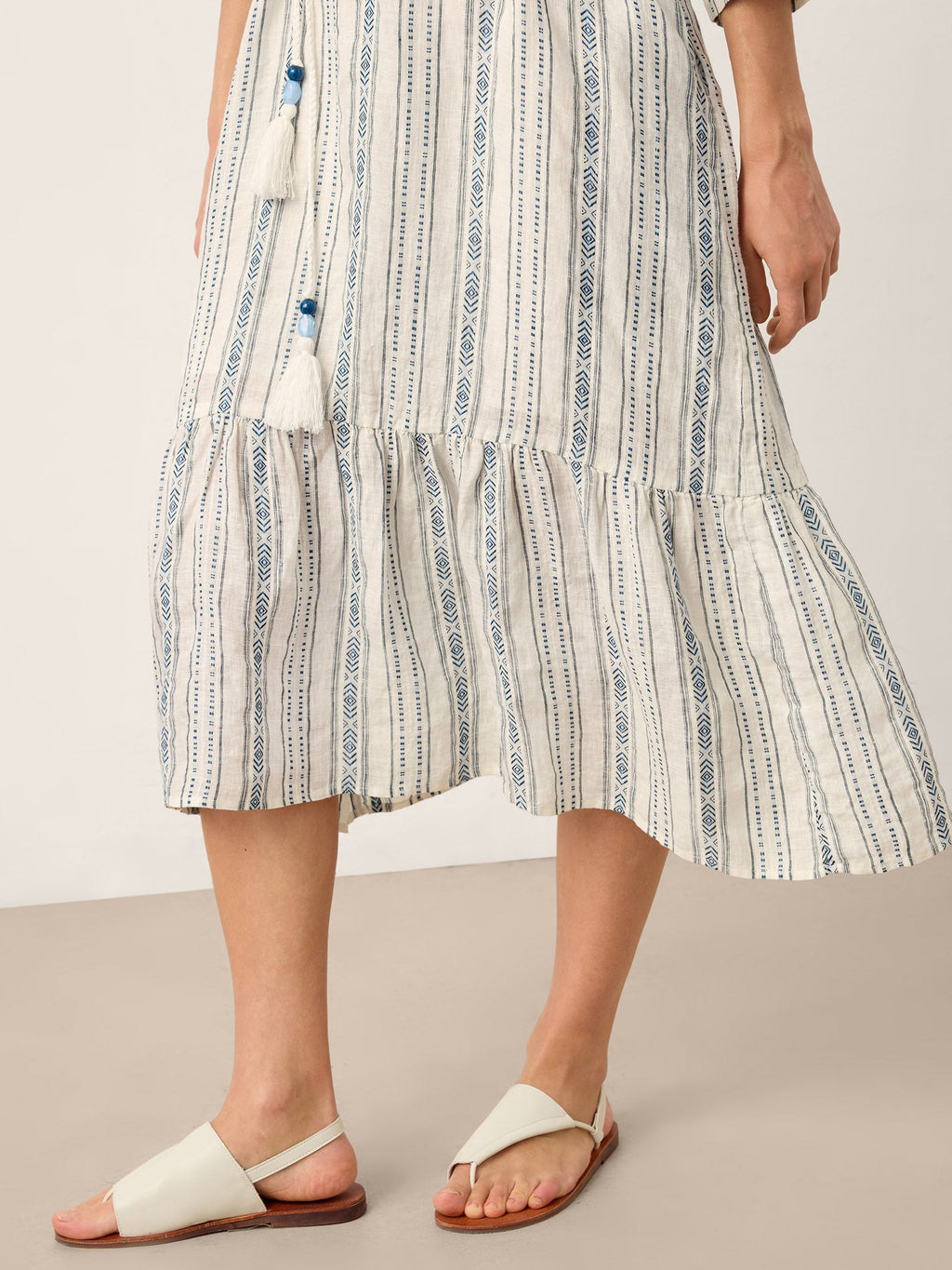Person wearing a striped dress with white sandals on a neutral background