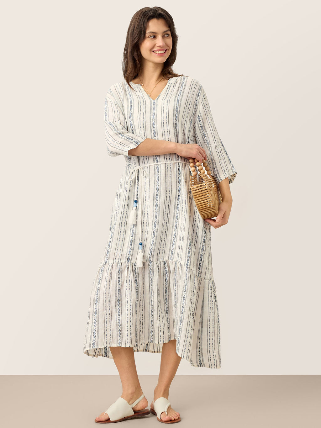 Woman wearing a striped dress holding a woven bag against a plain background