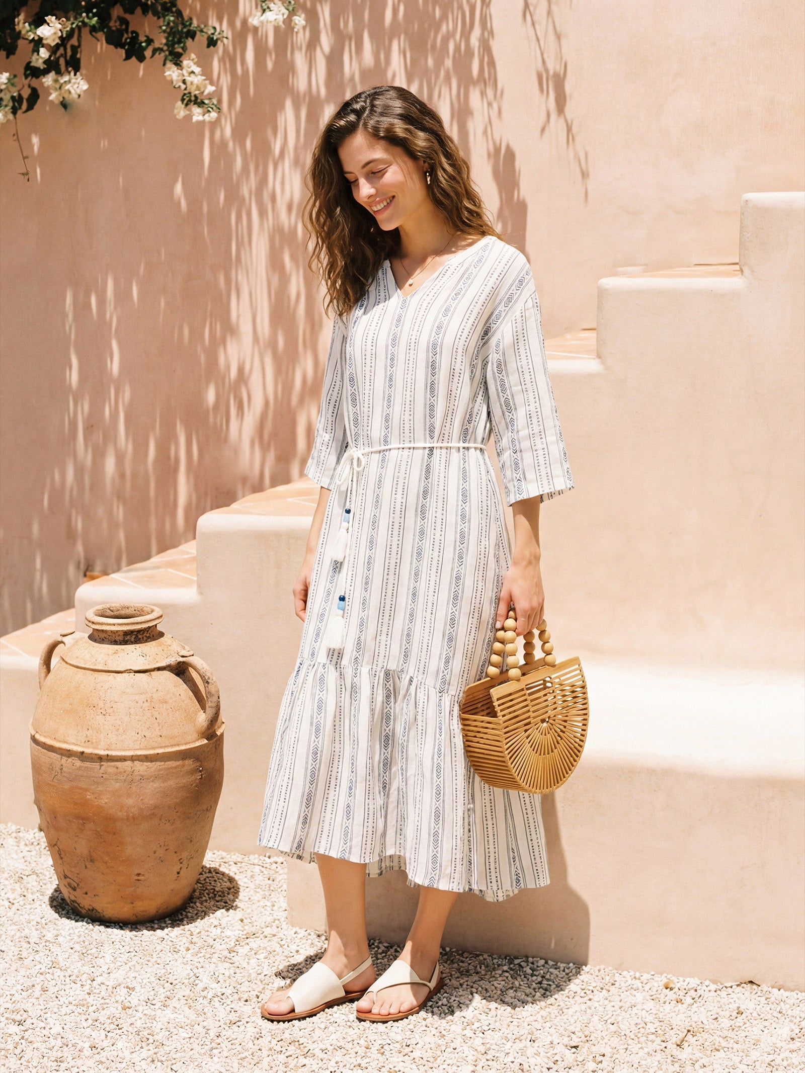 Woman in a striped dress standing outdoors with a textured wall and vase in the background