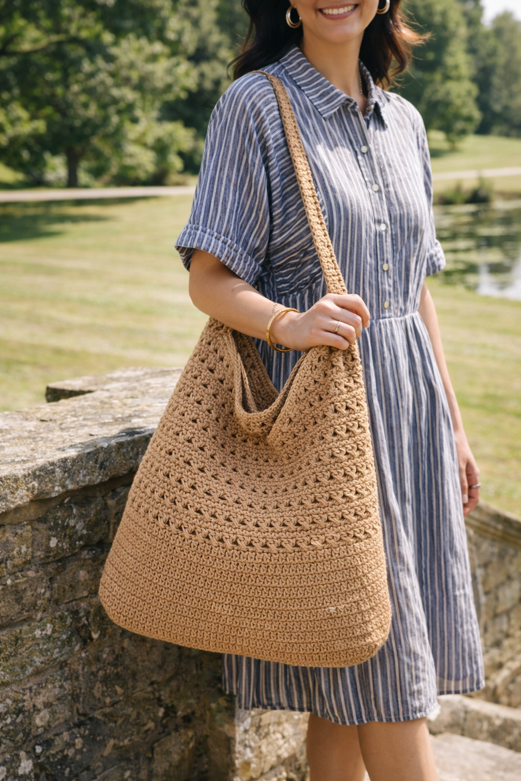 Woman in a striped dress holding a brown crochet bag outdoors.