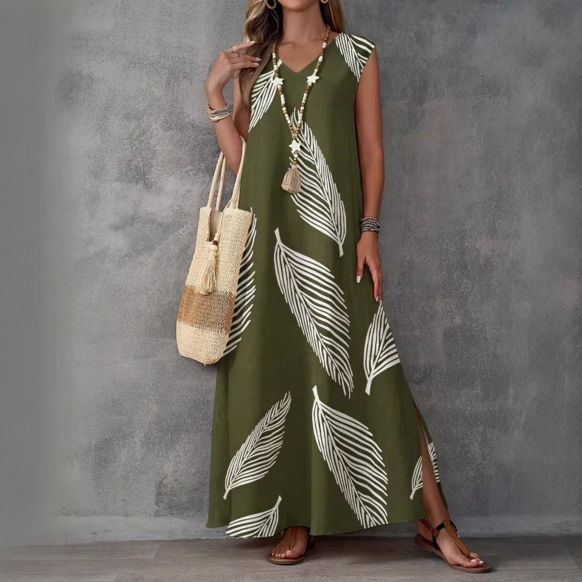 Woman wearing a green dress with white leaf patterns, holding a straw bag against a gray background.