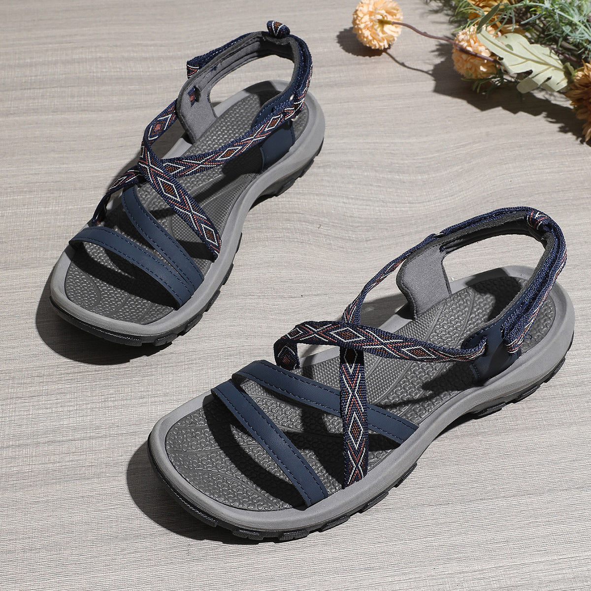 Pair of gray and navy sandals on a wooden surface with decorative elements.